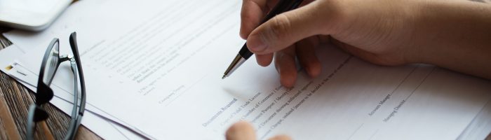 Unrecognizable businessman examining papers at table. Manager with ballpoint pen filling business papers. Close-up of male hands working at desk. Analyzing documents concept